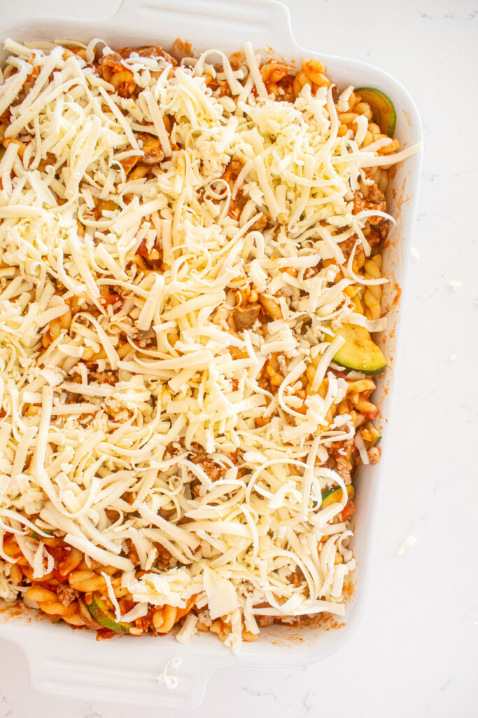 mushroom zucchini baked pasta in a white baking dish on a marble countertop ready to go into the oven.