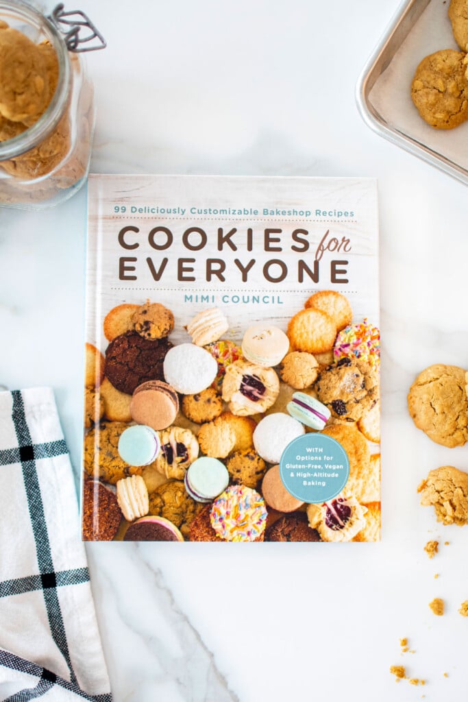 cookies for everyone cookbook on white marble countertop with peanut butter dog cookies on the side.