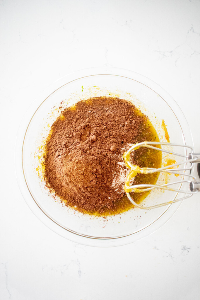 dry ingredients added to glass mixing bowl for pumpkin spice chocolate zucchini cake on a white marble countertop.