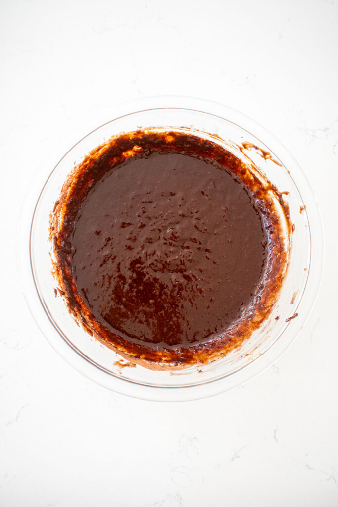 pumpkin spice chocolate zucchini cake batter in a glass mixing bowl on a white marble countertop.