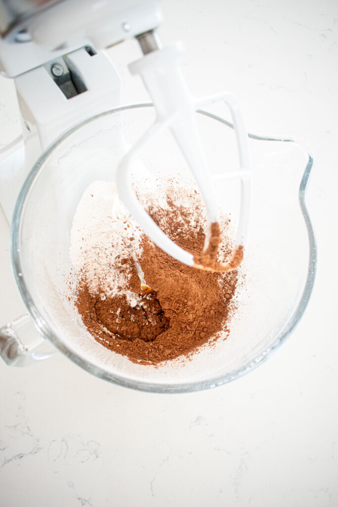 ingredients for chocolate frosting in a glass mixing bowl on a white marble countertop.