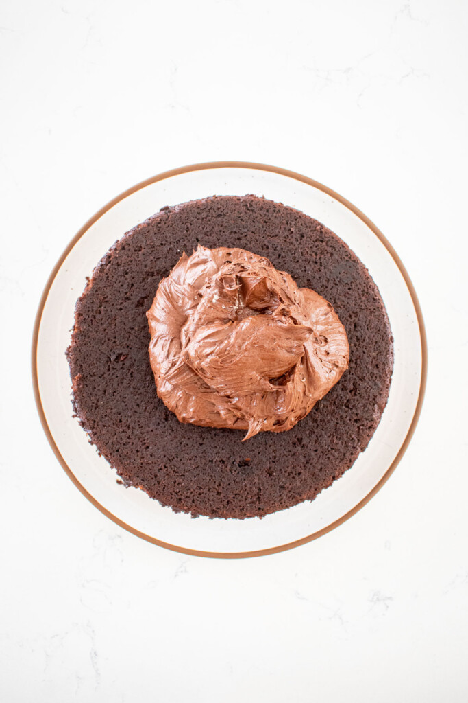 chocolate frosting on top of a pumpkin spice chocolate zucchini cake on a white marble countertop.