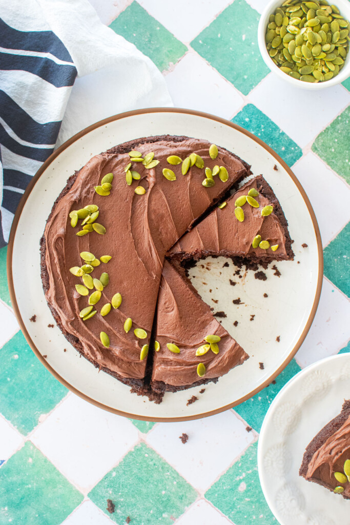 pumpkin spice chocolate zucchini cake cut into slices on a white plate on a green tile counter.