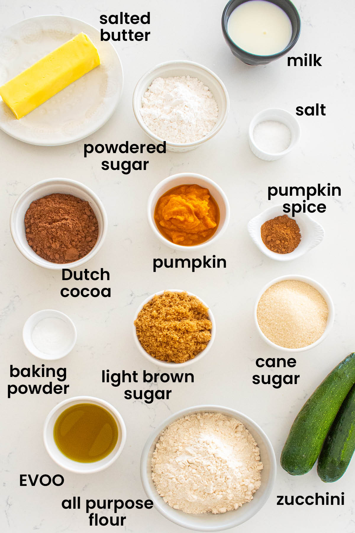 individual ingredients for pumpkin spice chocolate zucchini cake without eggs laid out against a white background.