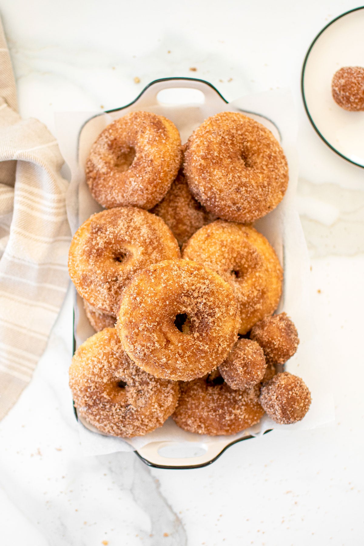 sparkling apple cider donuts in a white serving platter on a marble counter.