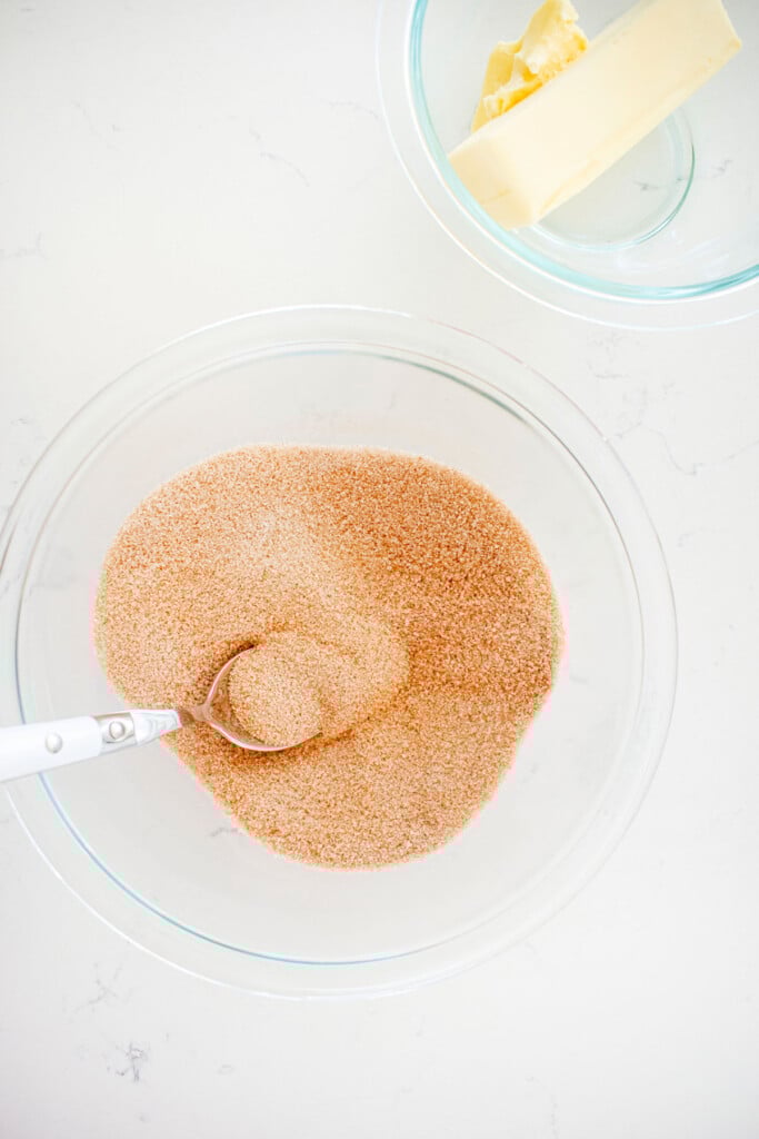 cinnamon and sugar mixed in a glass mixing bowl on a white marble counter.