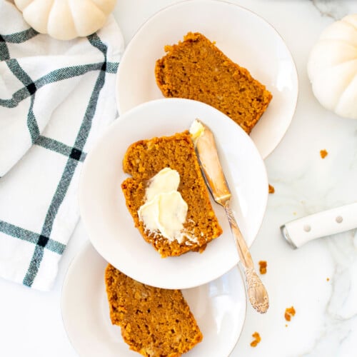 slices of vegan pumpkin spice banana bread on white plates on a white marble counter.
