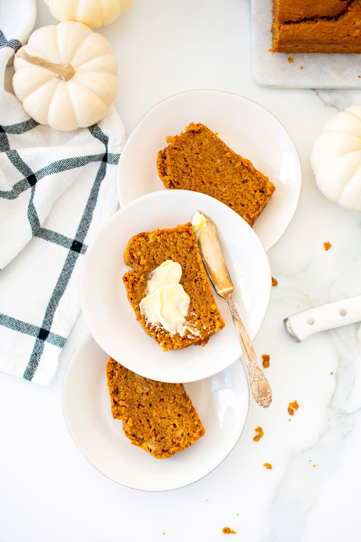 slices of vegan pumpkin spice banana bread on white plates on a white marble counter.