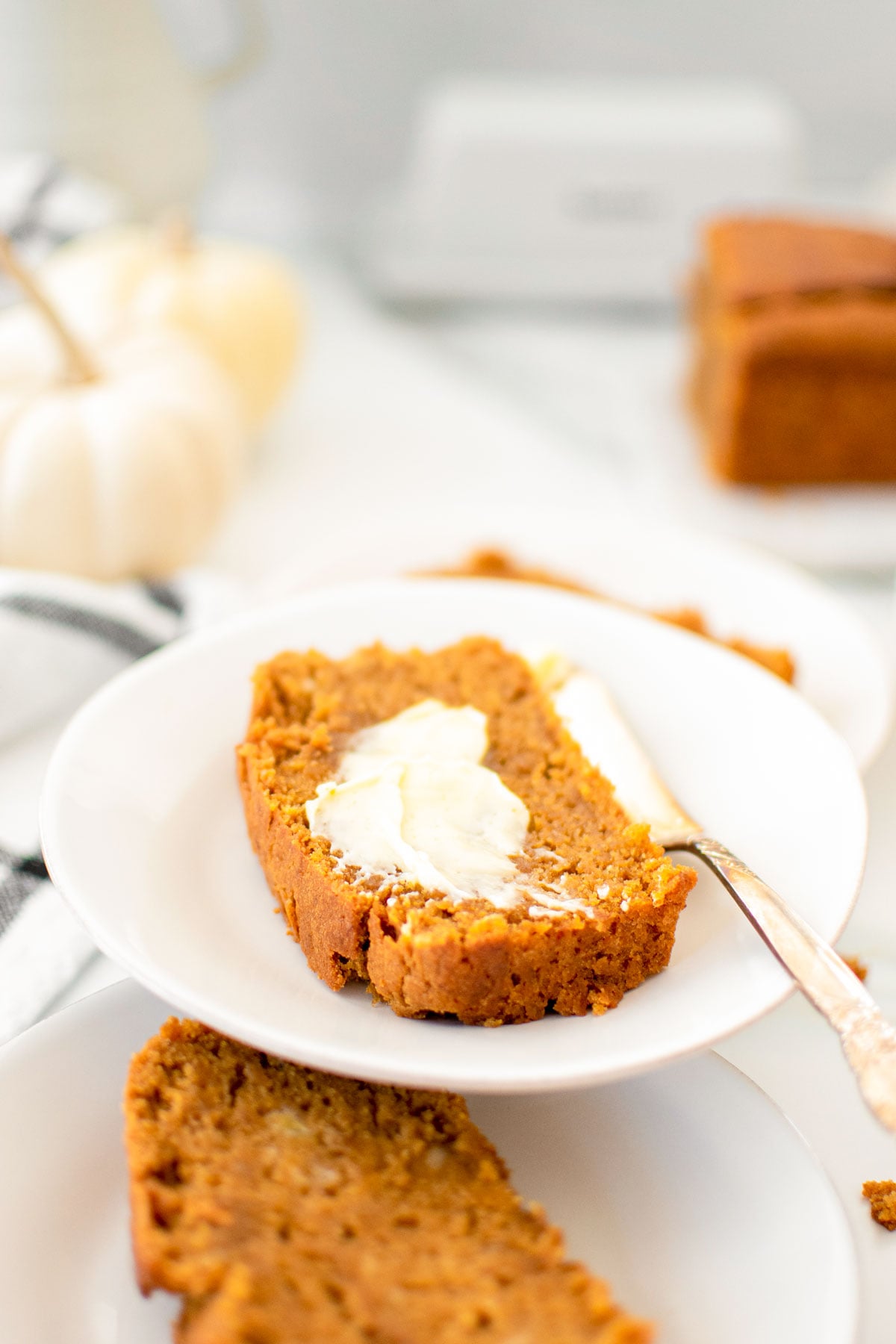 slices of vegan pumpkin spice banana bread on white plates on a white marble counter.