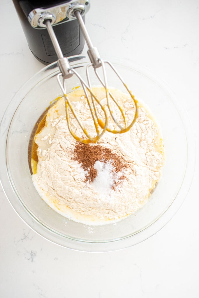 ingredients for pumpkin spice banana bread in a glass mixing bowl on a marble counter.