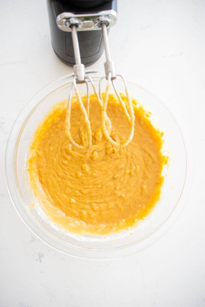 vegan pumpkin spice banana bread in a glass mixing bowl on a marble counter with a hand mixer.
