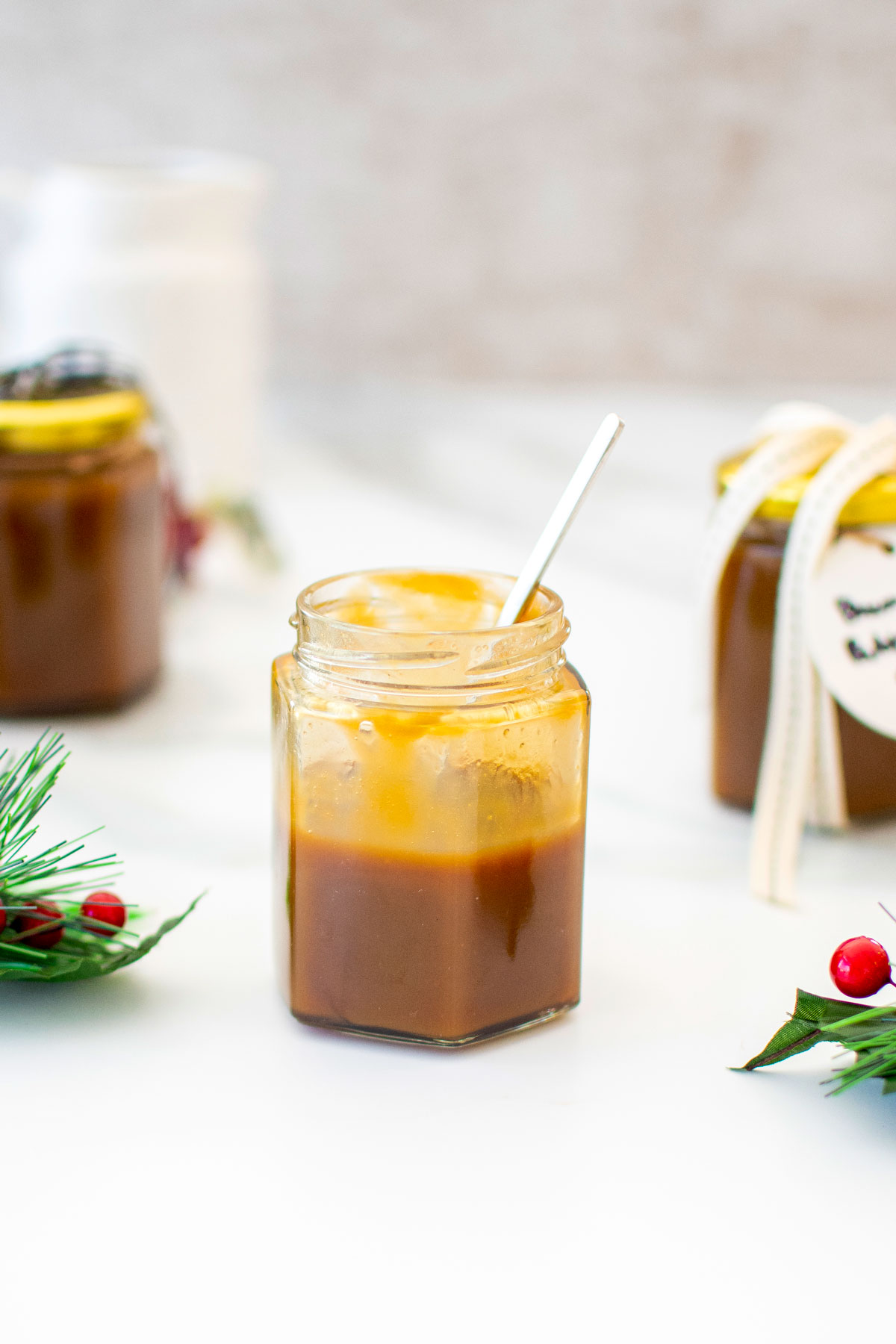 glass jar of brown butter butterscotch sauce with a spoon in it on a white marble counter.