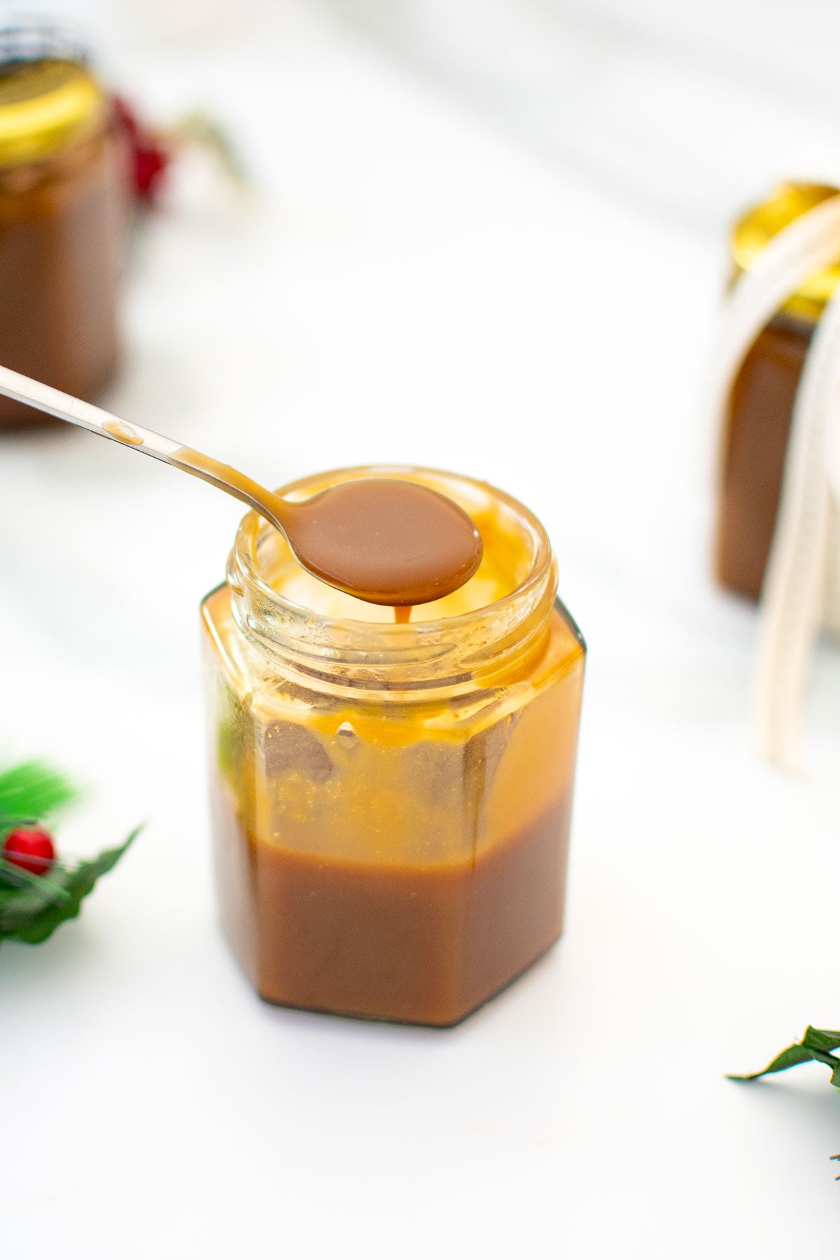 glass jar of brown butter butterscotch sauce with a spoon in it on a white marble counter.
