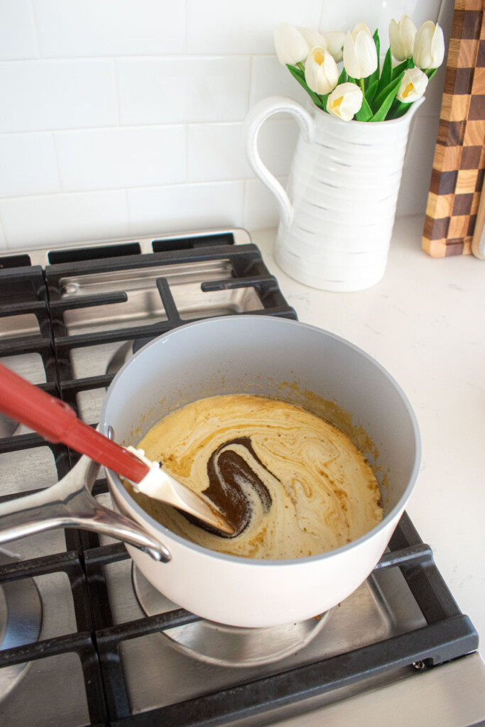 cream being added to brown butter butterscotch sauce being stirred on the stovetop.