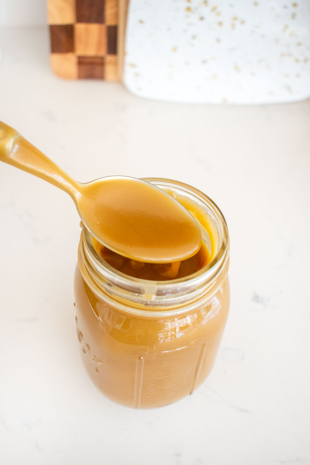 brown butter butterscotch sauce being spooned out of a mason jar on a white marble counter.