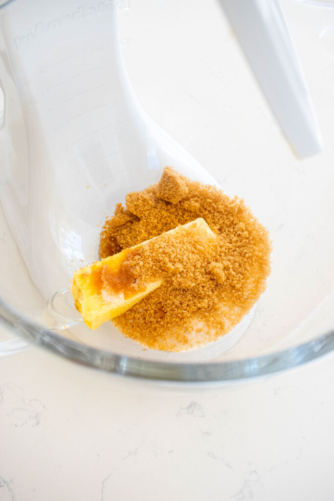 butter and sugar in a glass mixing bowl on a white marble counter.