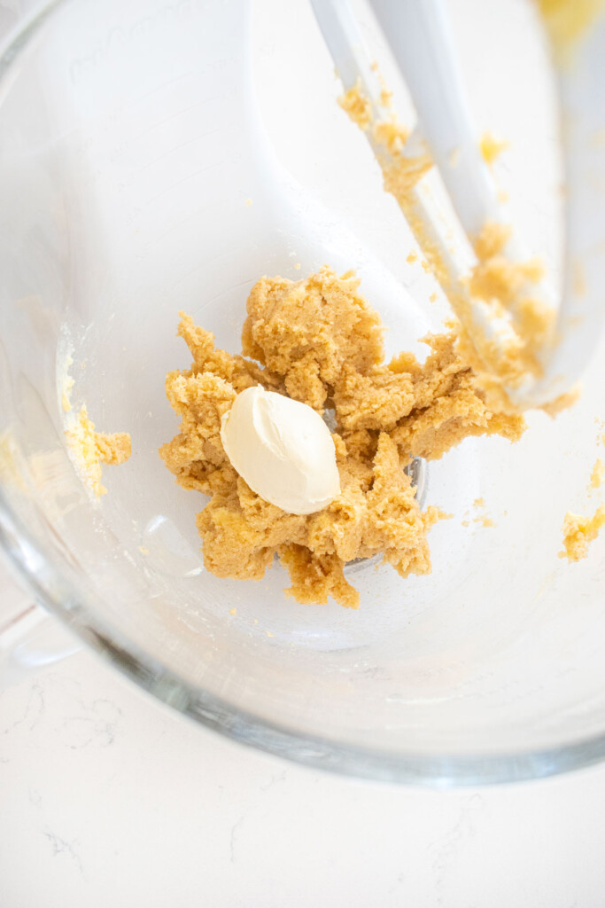 creamed butter and sugar with cream cheese in a glass mixing bowl on a white marble counter.