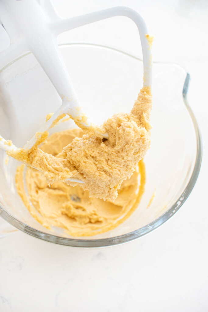 creamed butter and sugar in a glass mixing bowl on a white marble counter.