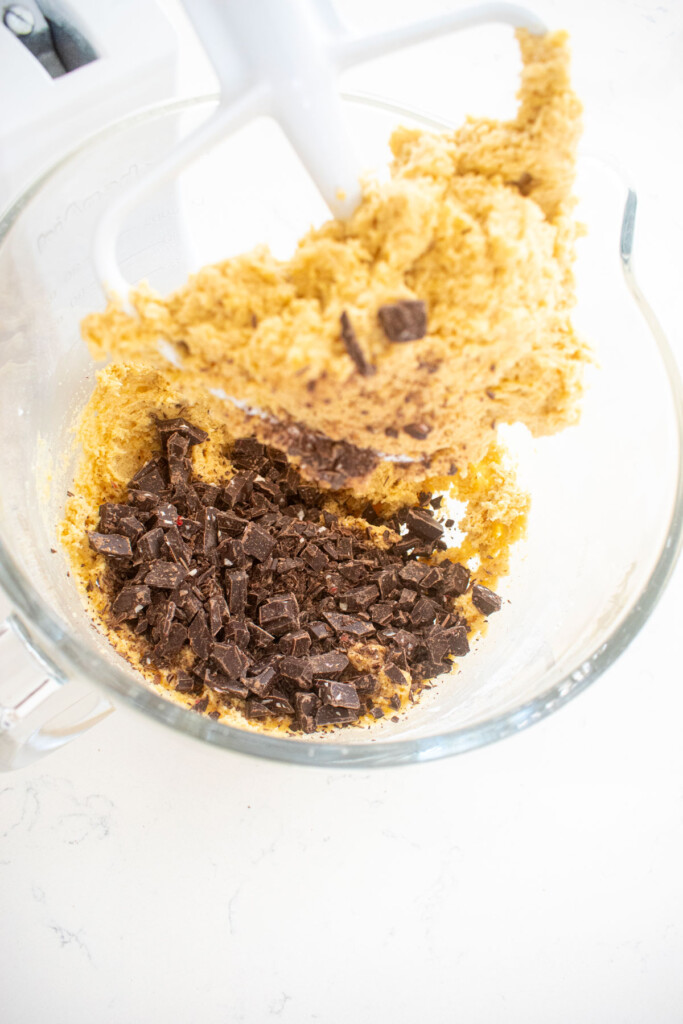 candy cane crunch dark chocolate cookie dough in a glass mixing bowl on a white marble counter.
