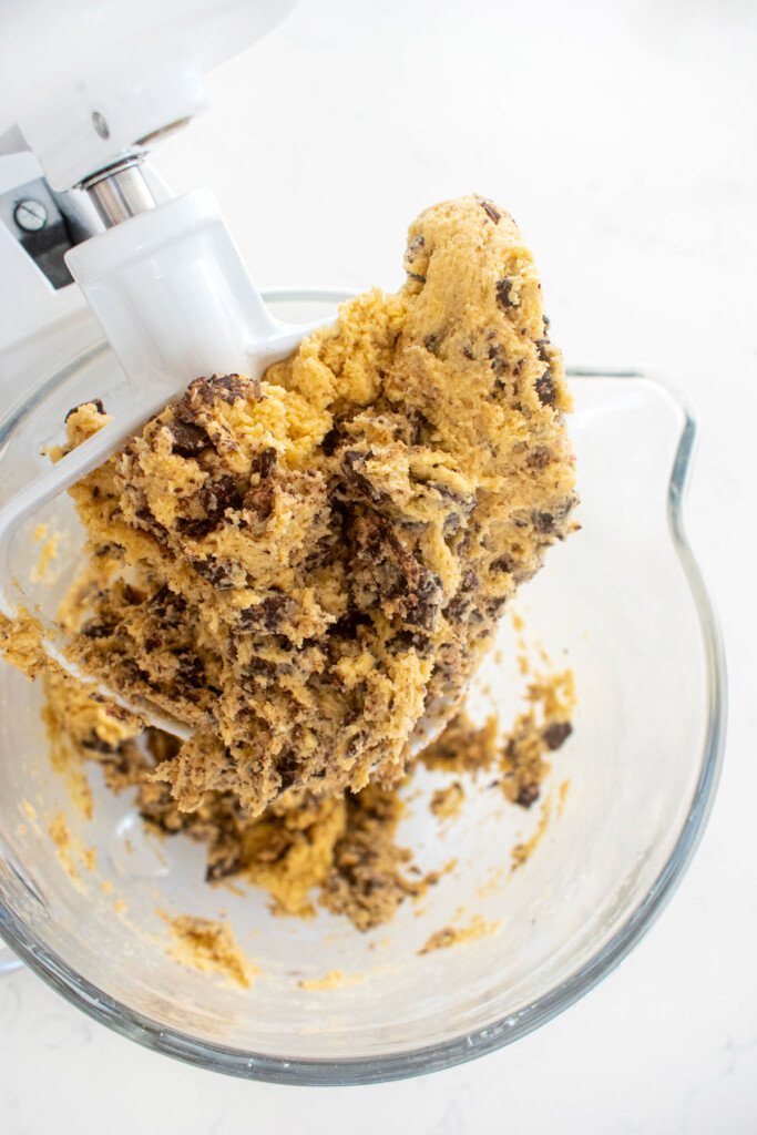 candy cane crunch dark chocolate cookie dough in a glass mixing bowl on a white marble counter.