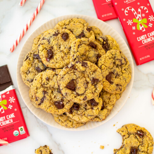 plate of candy cane crunch dark chocolate cookies on a white marble counter with candy canes and chocolate bars.