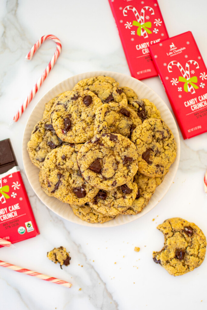 plate of candy cane crunch dark chocolate cookies on a white marble counter with candy canes and chocolate bars.