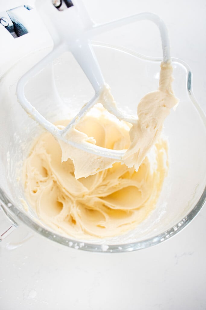 cream cheese frosting in a glass mixing bowl on a white marble counter.