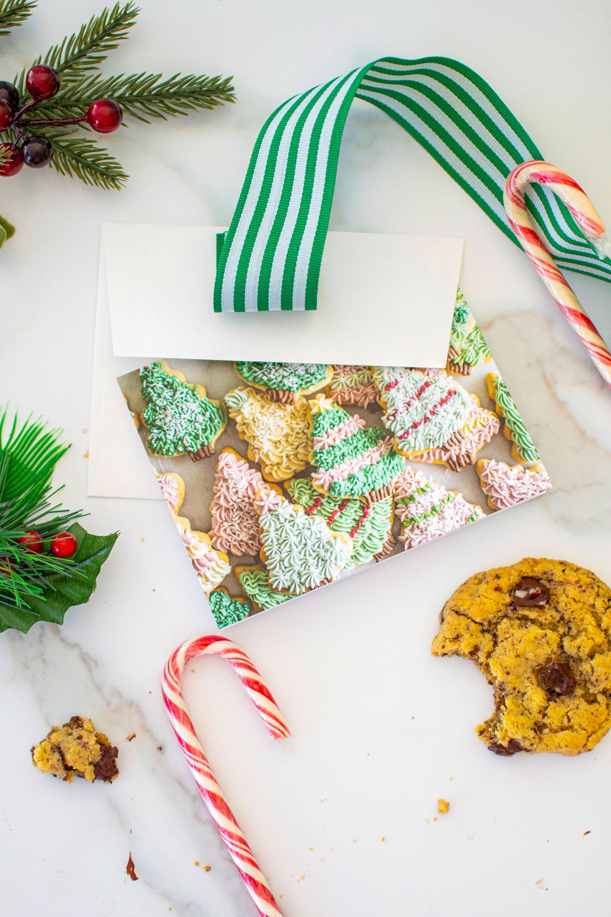 holiday card with ribbon, candy cane and a cookie on a white marble counter.