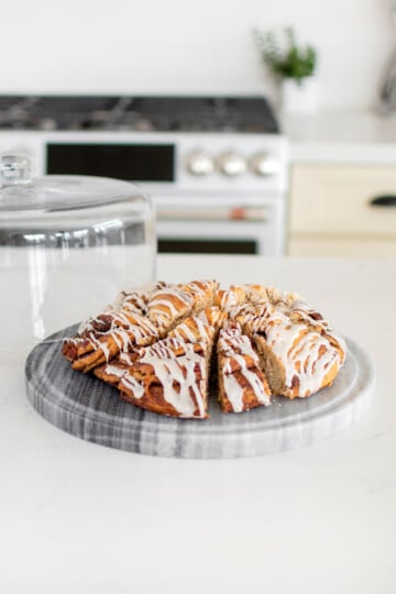 cinnamon pecan babka coffee cake with glaze sliced in a cake dome on a white marble counter.