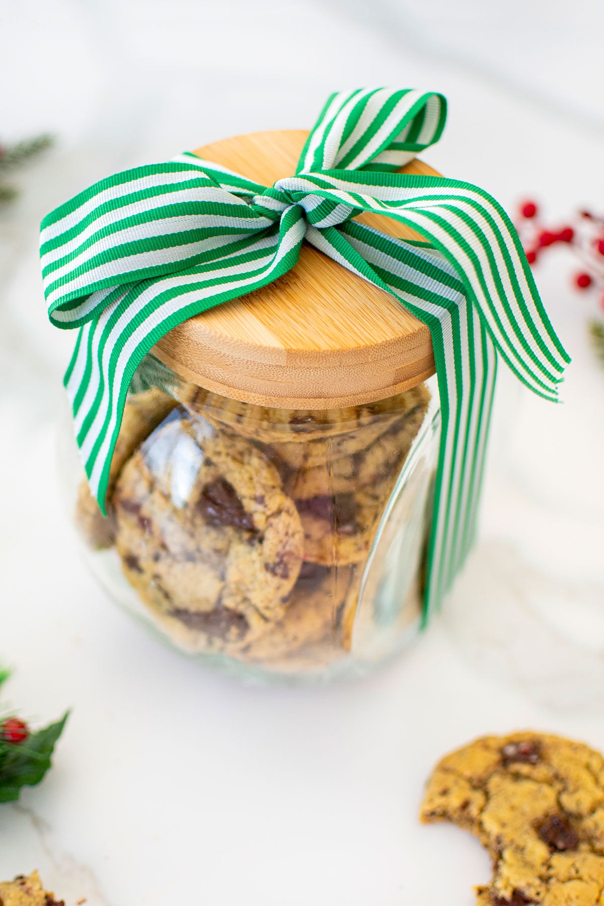 glass cookie jar with a wood lid and a green and white ribbon tied around it on a white marble counter.