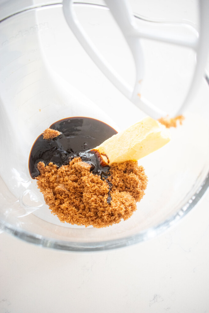 butter sugar and molasses in a glass mixing bowl on a white marble counter.