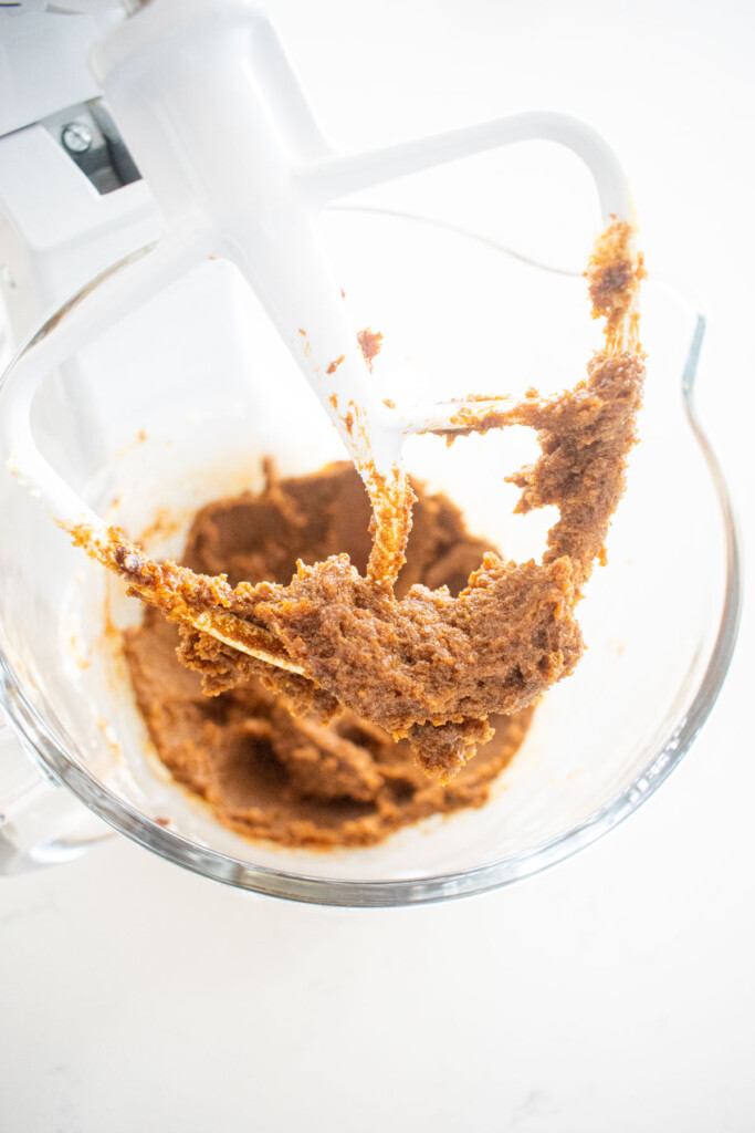 creamed butter sugar and molasses in a glass mixing bowl on a white marble counter.