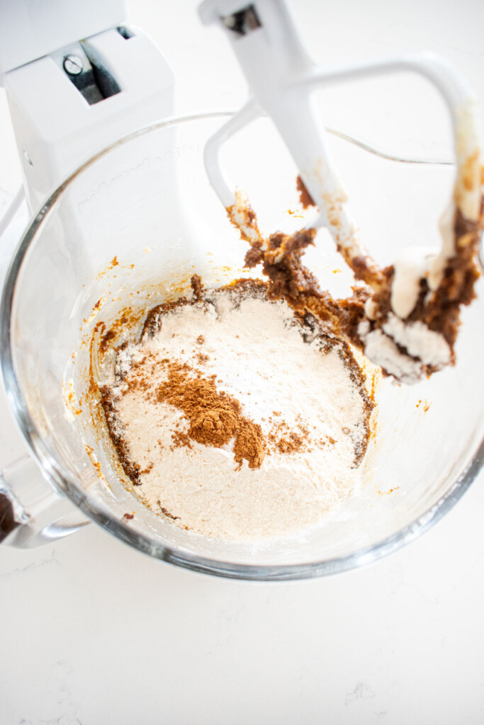 ingredients for eggless sourdough molasses cookies in a glass mixing bowl on a white marble counter.