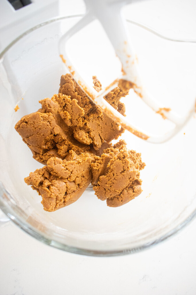 eggless sourdough molasses cookie dough in a glass mixing bowl on a white marble counter.