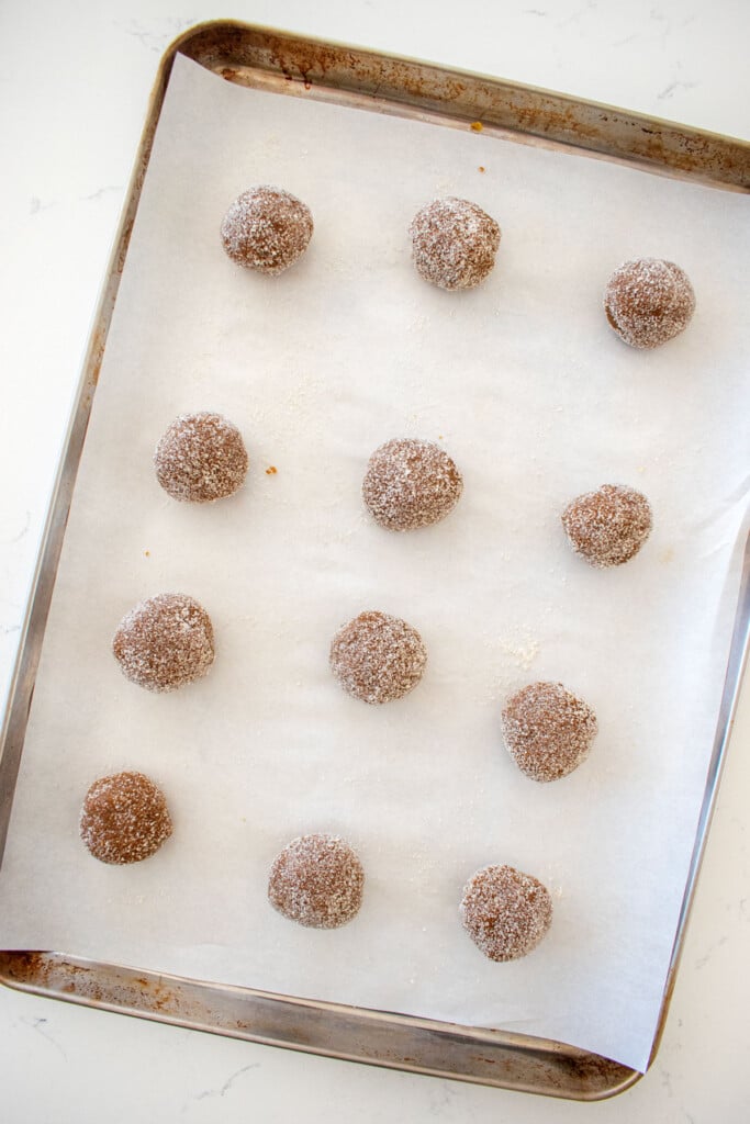 eggless sourdough molasses cookie dough balls rolled in cane sugar spread out evenly on a baking sheet on a white marble counter.