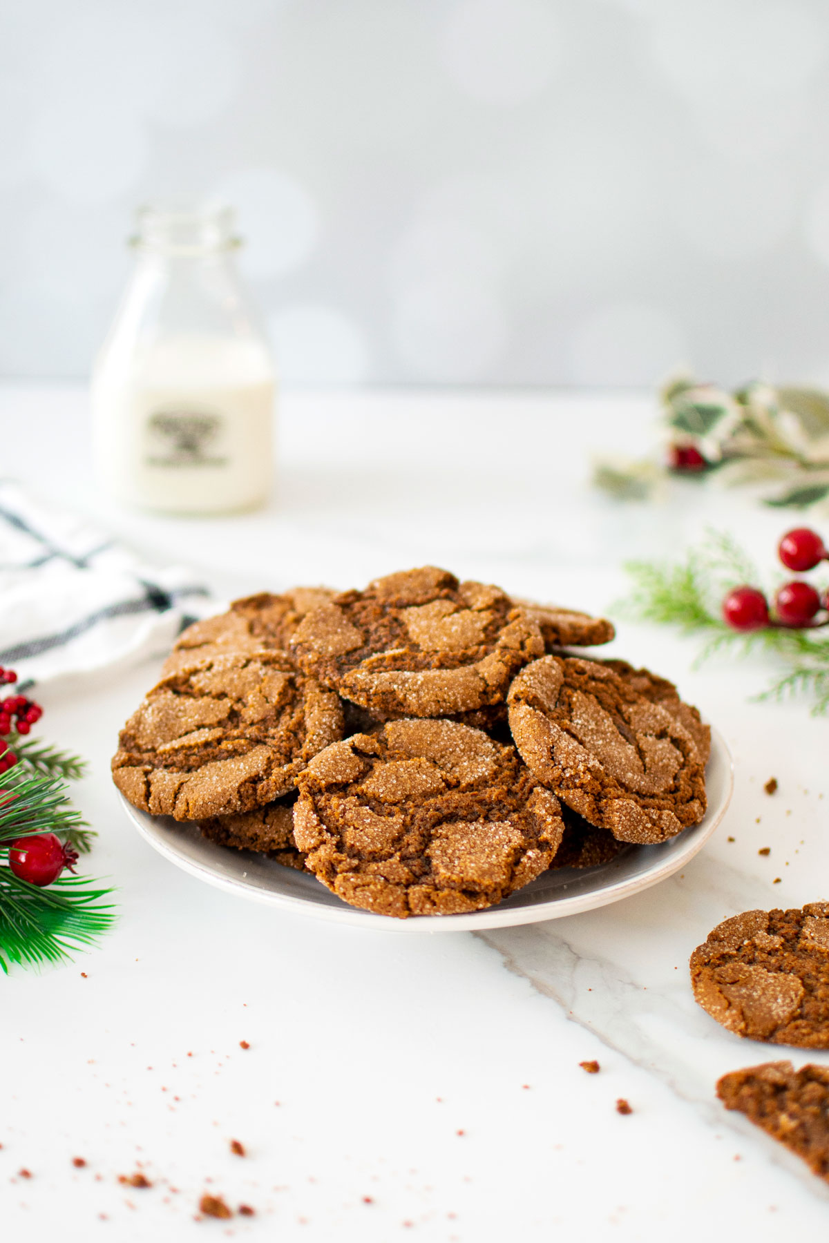 plate of eggless sourdough molasses cookies on a white marble counter with a glass jug of milk.