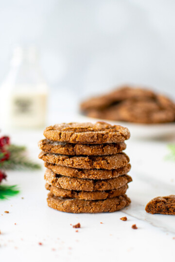 stack of eggless sourdough molasses cookies on a white marble counter with a glass jug of milk.
