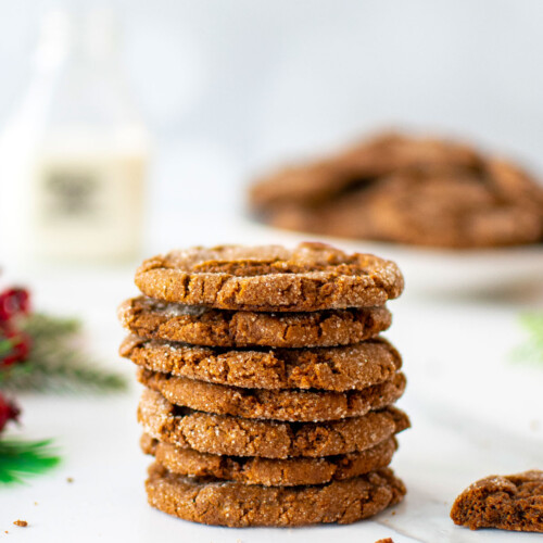 stack of eggless sourdough molasses cookies on a white marble counter with a glass jug of milk.