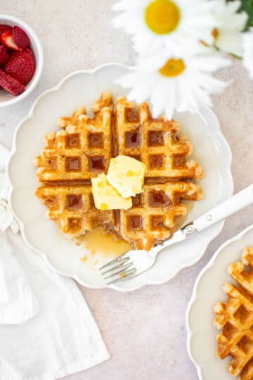 eggless sourdough waffles on a white plate with butter and maple syrup.