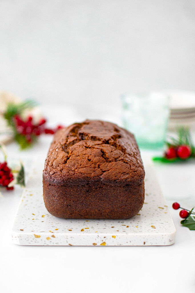 frosted gingerbread banana bread on a marble serving board on a marble counter with holiday greens around.