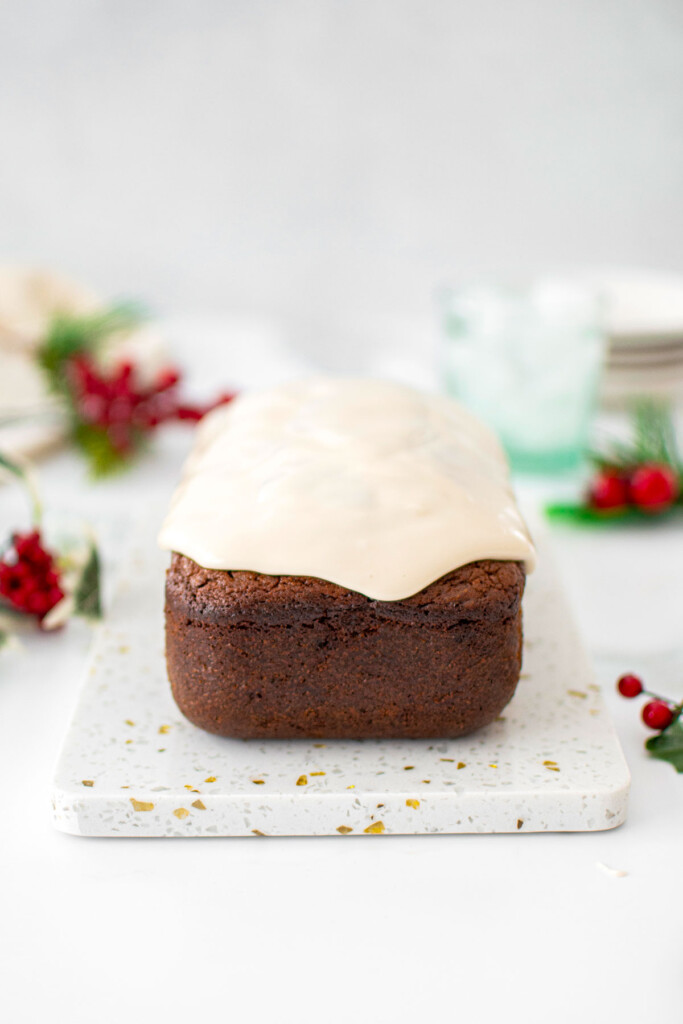 frosted gingerbread banana bread on a marble serving board on a marble counter with holiday greens around.