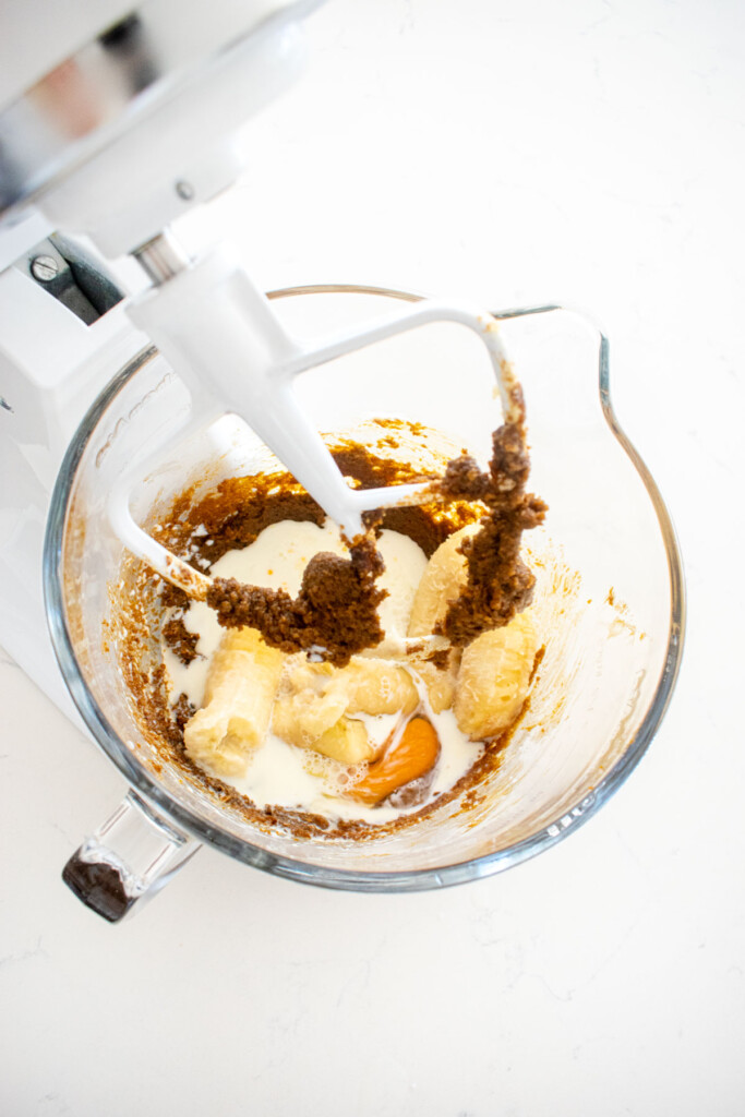 ingredients for frosted gingerbread banana bread in a glass mixing bowl on a white marble counter.