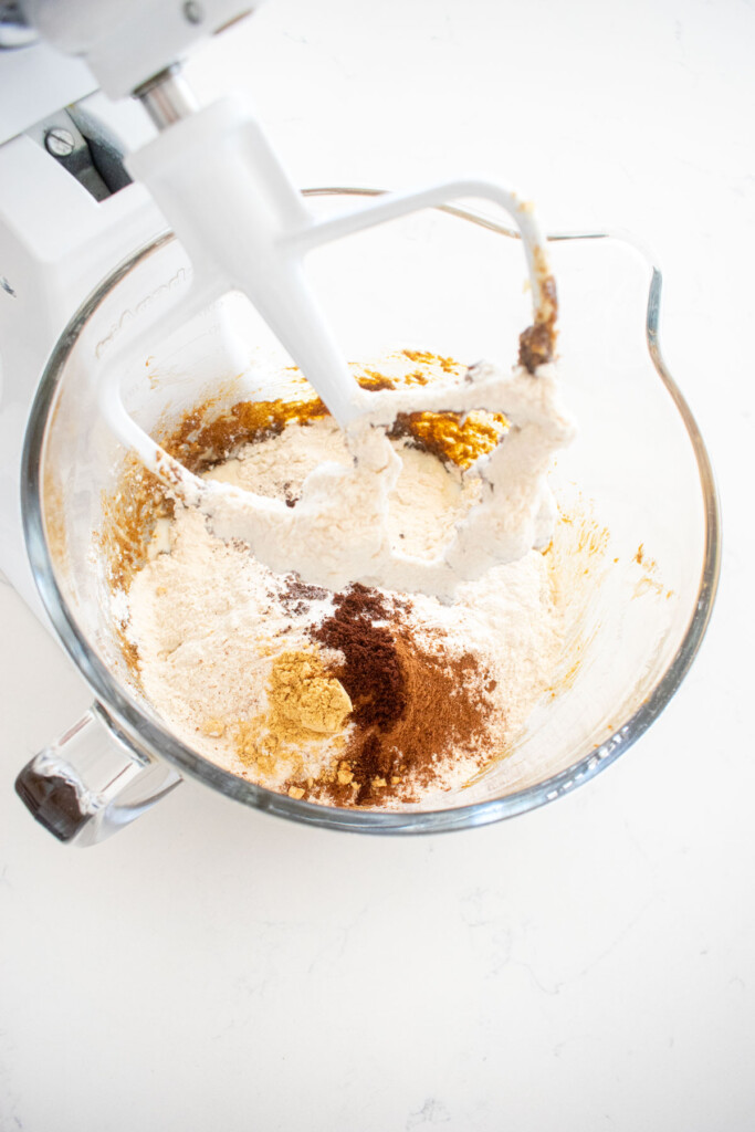 frosted gingerbread banana bread in a glass mixing bowl on a white marble counter.