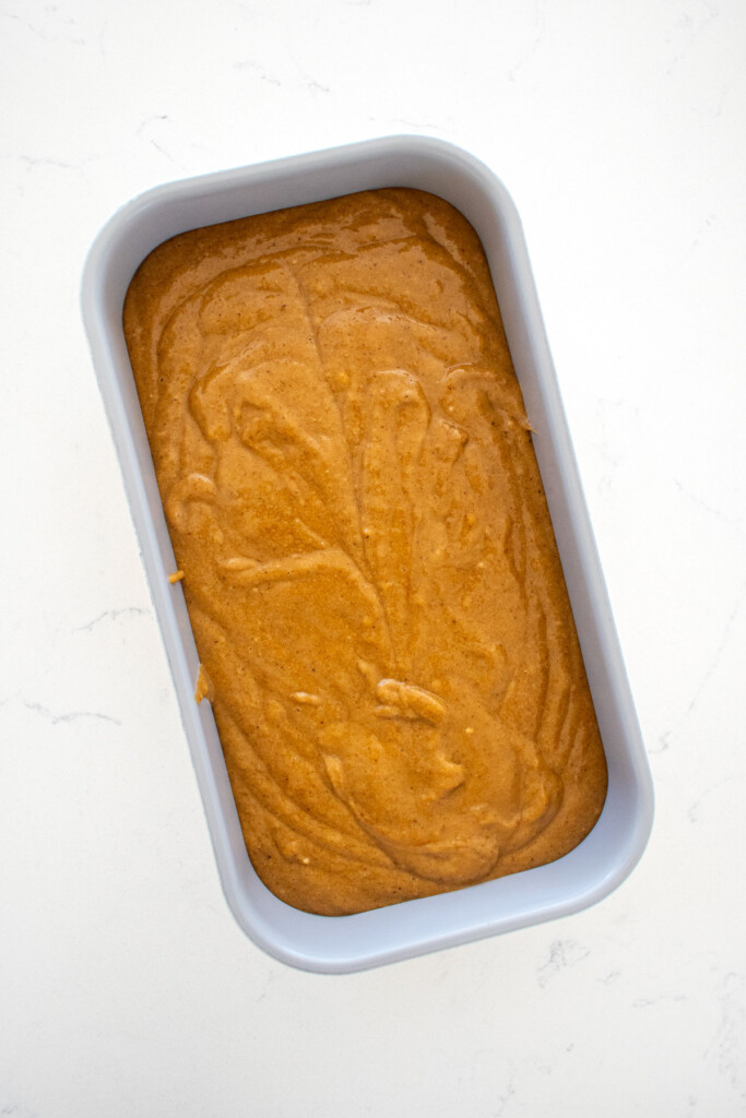 gingerbread banana bread batter in a loaf pan on a white marble counter.
