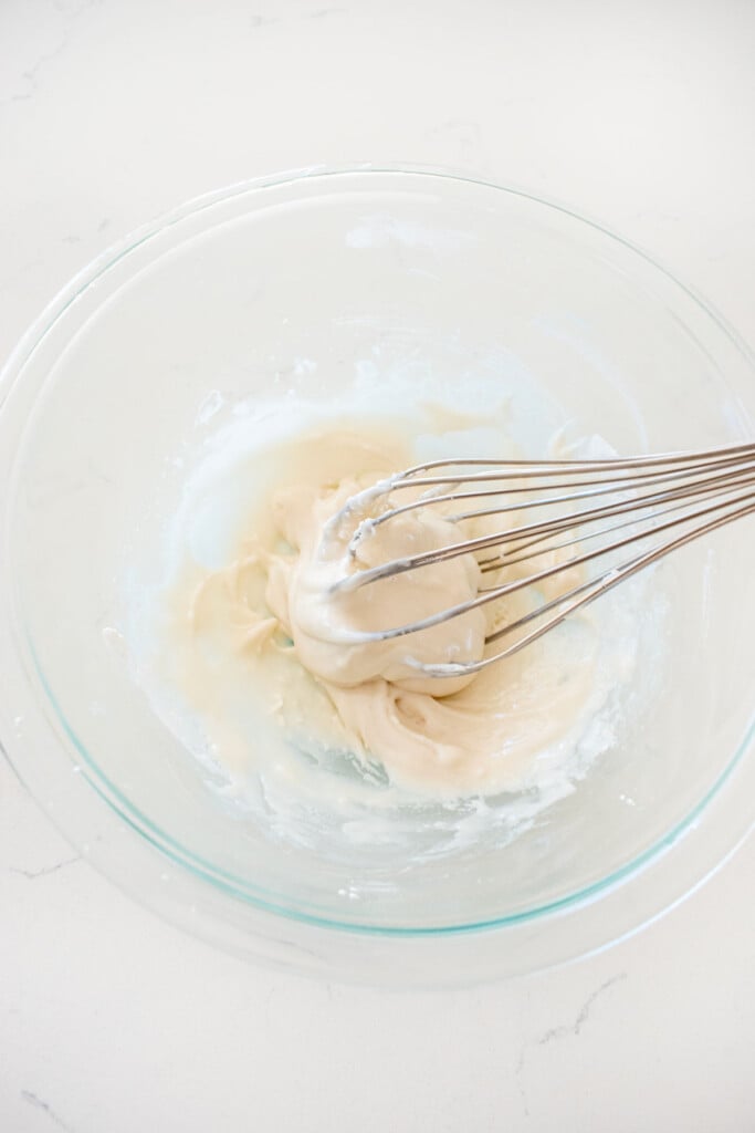 glaze in a glass mixing bowl with a whisk on a white marble counter.