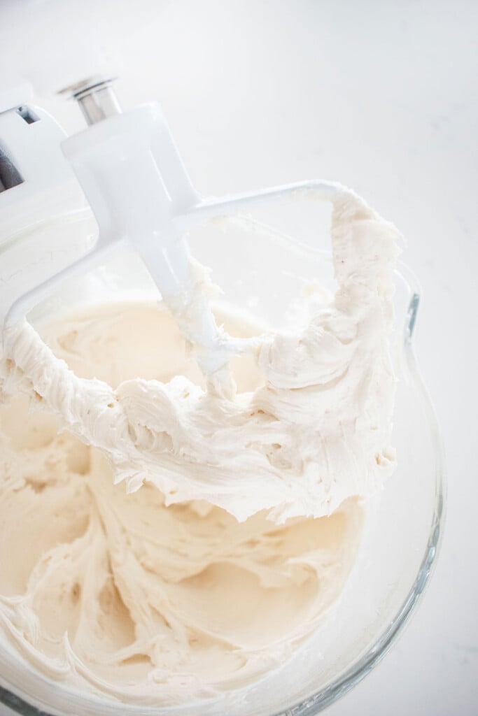 buttercream frosting in a mixing bowl on a white marble counter.