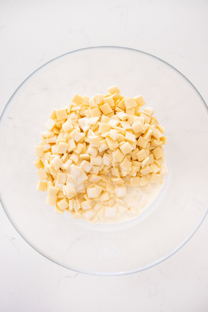 white chocolate and cream in a glass mixing bowl on a white marble counter.