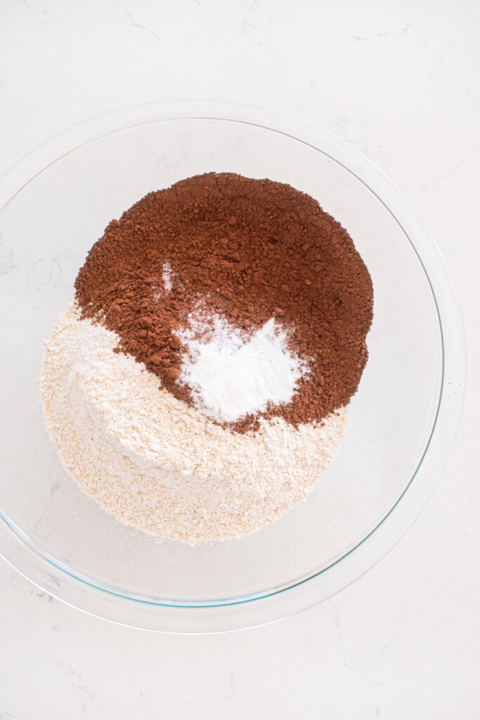 dry ingredients for chocolate cake in a glass mixing bowl on a white marble counter.