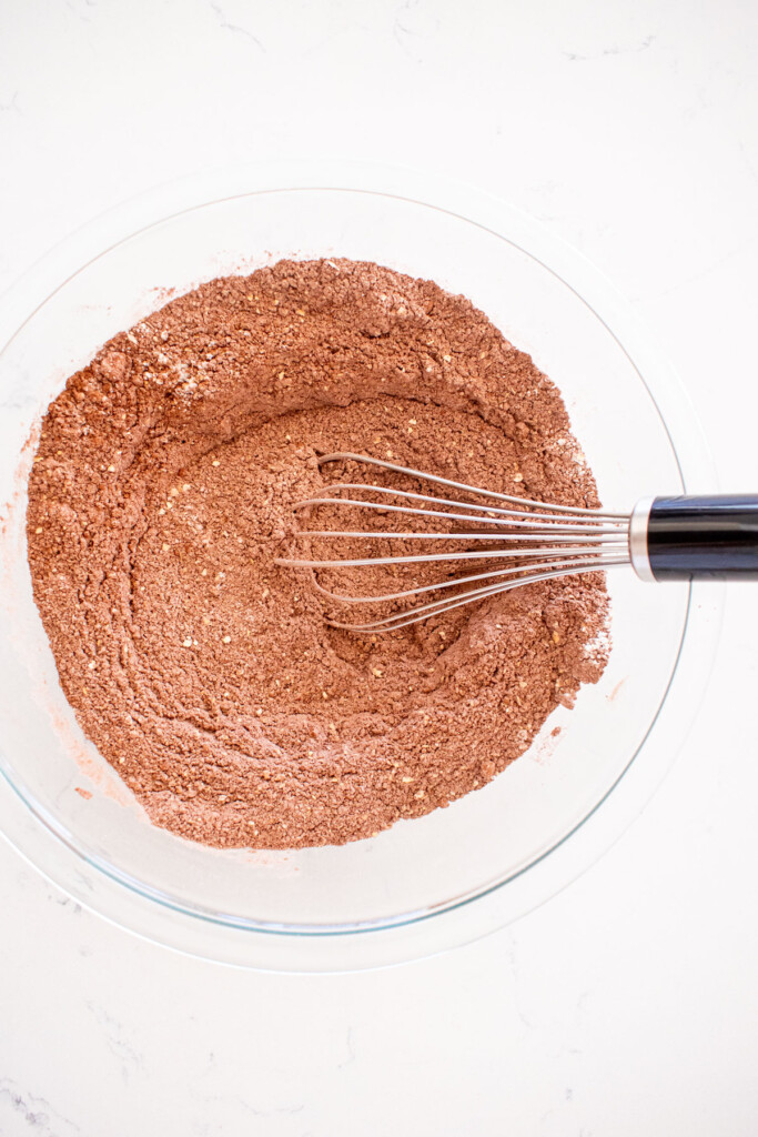 dry ingredients for chocolate cake batter in a glass mixing bowl on a white marble counter.