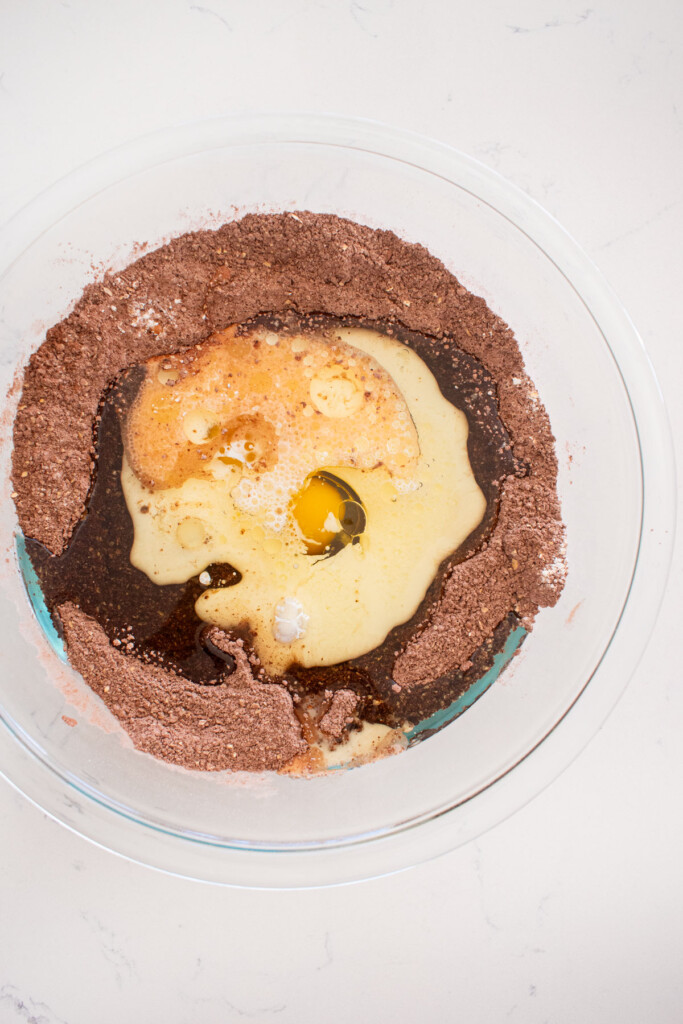 ingredients for chocolate cake in a glass mixing bowl on a white marble counter.